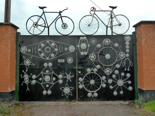 A black gate decorated with bicycle parts, with two bicycles mounted on top, near Kilcock